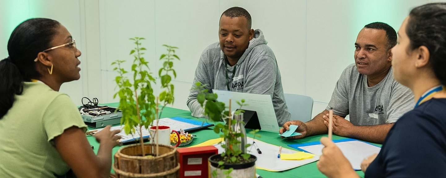 Four participants discuss their work around a table with worksheets, pens and materials at a Movimento Circular workshop.
