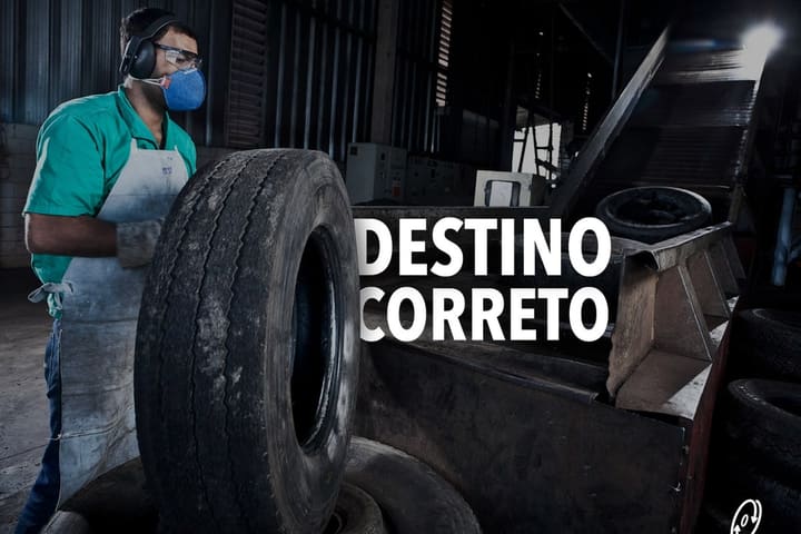 Trabalhador de máscara e luvas empilha pneus usados num galpão, sob o mote Destino Correto.