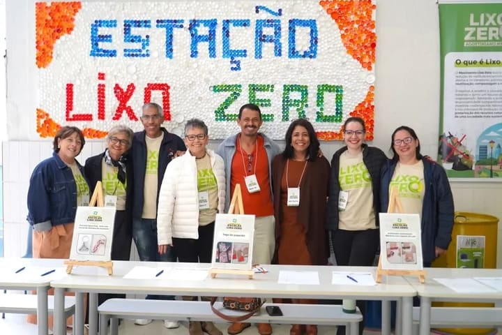 Equipe do Klíma diante do painel Estação Lixo Zero feito de tampinhas, numa escola.