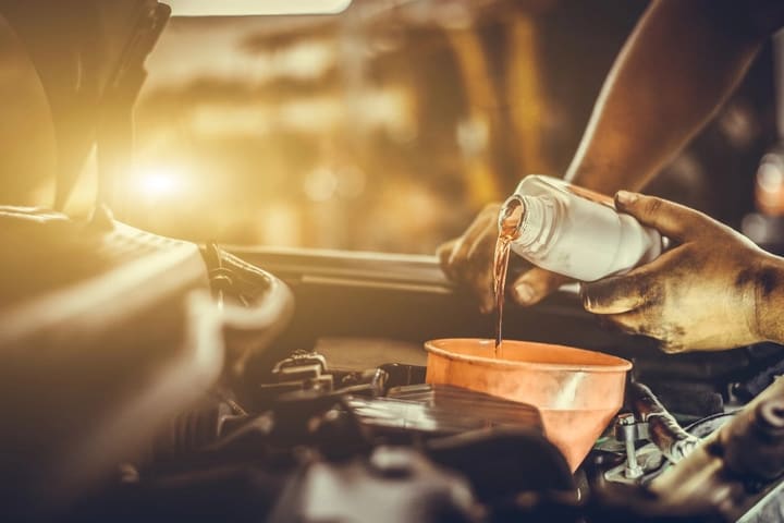 Mão despeja óleo lubrificante num funil sobre o motor de um veículo.