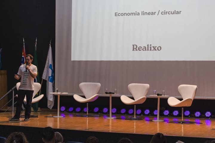 Apresentador da Realixo no palco do II Fórum, com o telão sobre economia linear e circular.