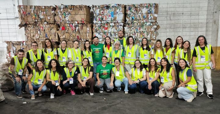 Participantes da visita técnica à Coopercaps reunidos em frente a fardos de materiais recicláveis