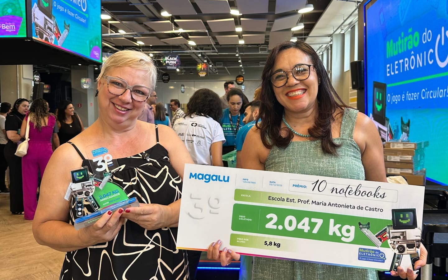 Two adult participants hold a trophy and an award board at Magalu’s Mutirão do Eletrônico.